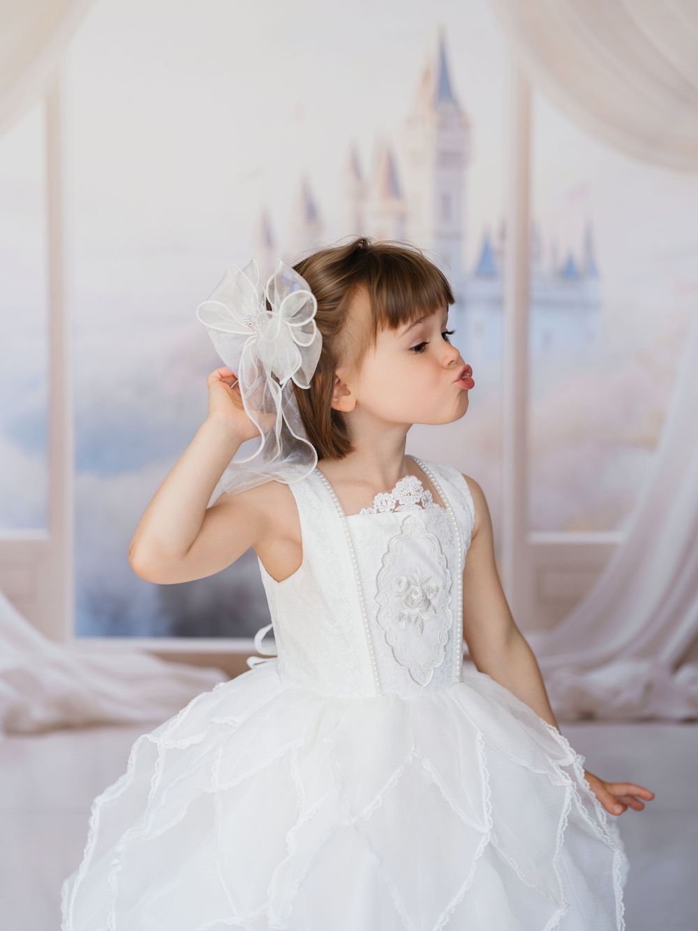 A figure in a white flowing dress dances gracefully against a light backdrop in a dreamy studio setting.
