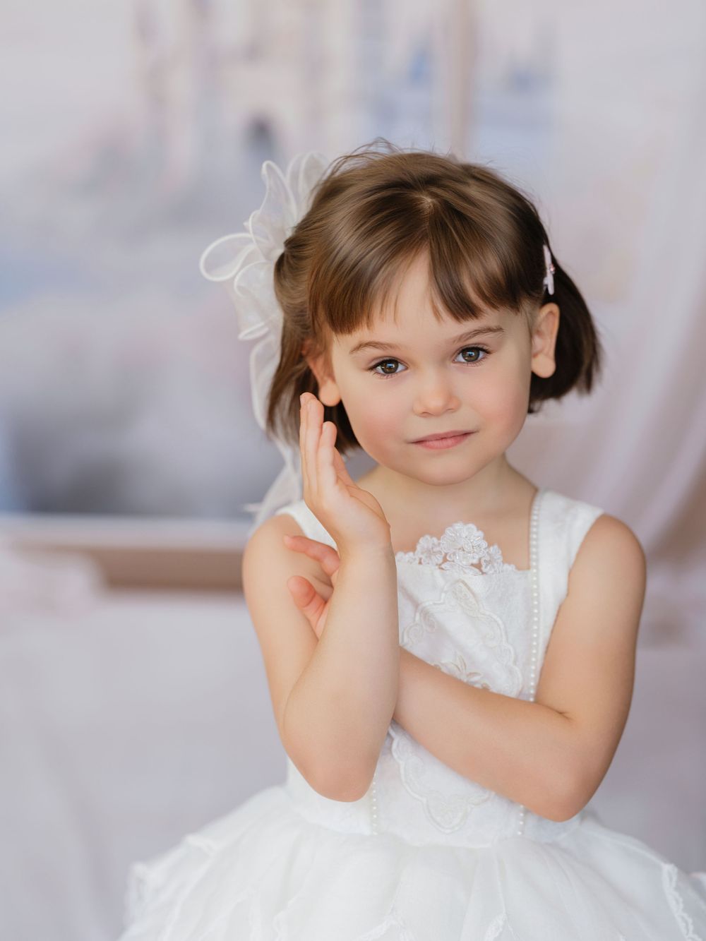 A charming young person in a white lace dress elegantly poses in a bright studio setting.