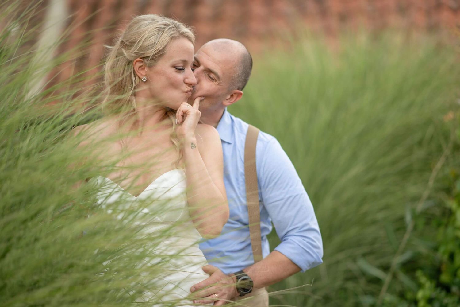 A romantic wedding couple embraces in tall swaying grass on a summer day.
