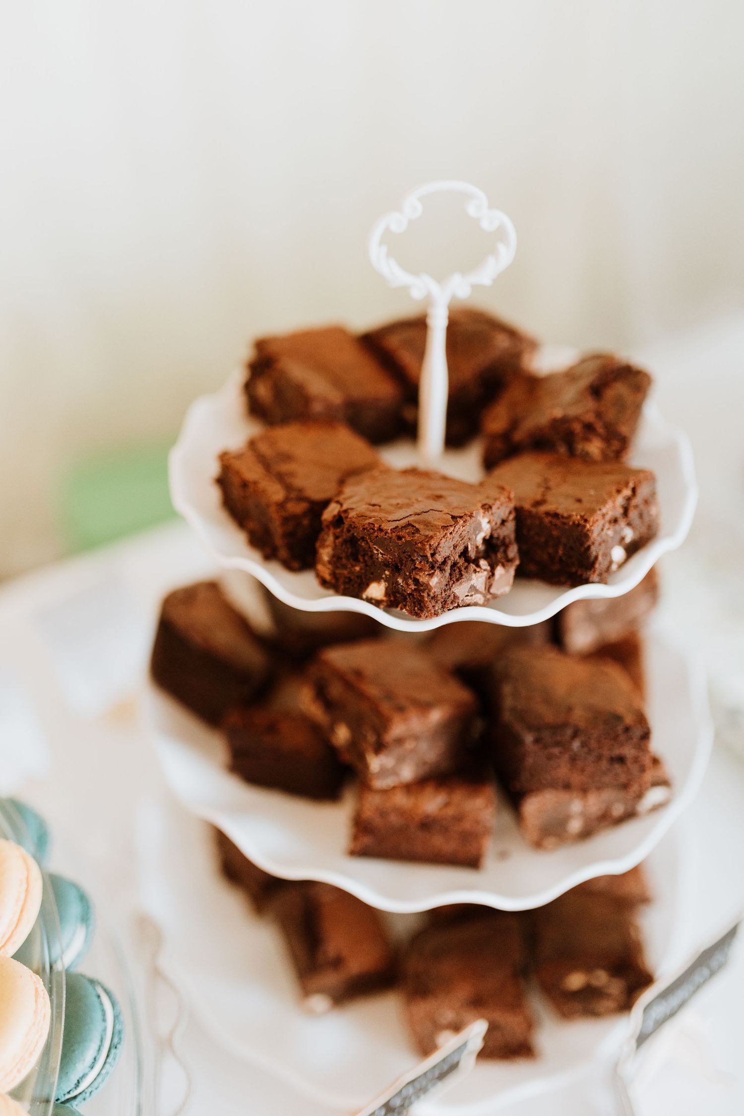 Rich chocolate brownies displayed on an elegant three-tiered white serving stand with scalloped edges.