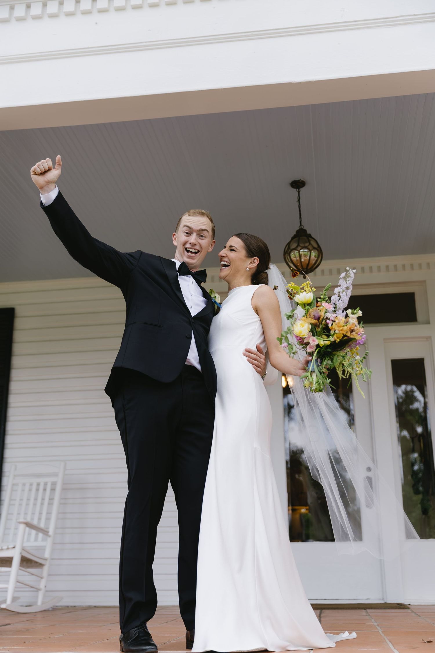 Black and white photo of a joyful wedding couple embracing and dancing outdoors with string lights in the background.