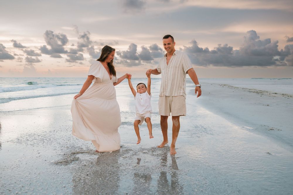 Family in white outfits plays together on a beach at sunset while walking along the shoreline.