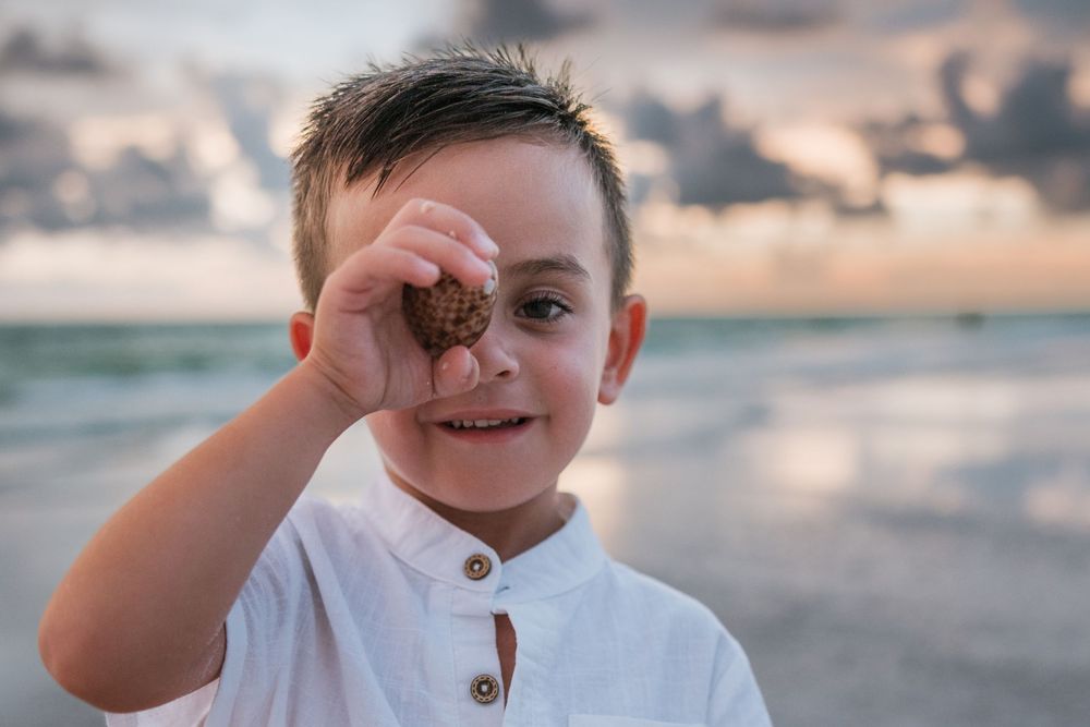 Child with beach waves holding chocolate cookie to their forehead creates fun, playful moments by the ocean.