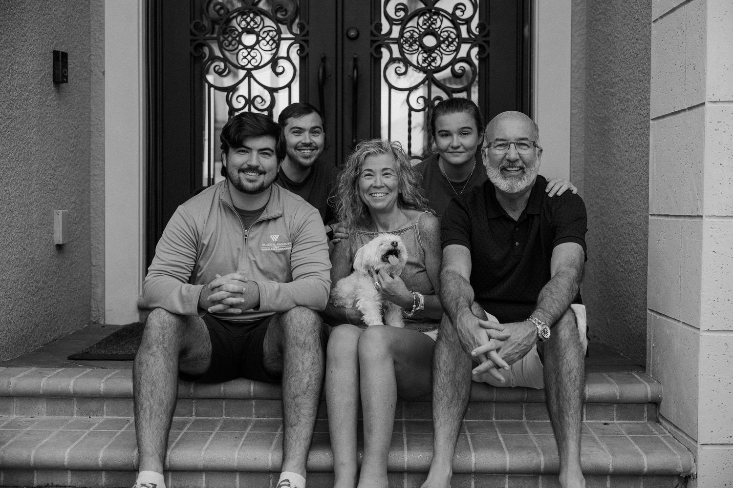 Family members sit and smile together on front porch steps of a house.