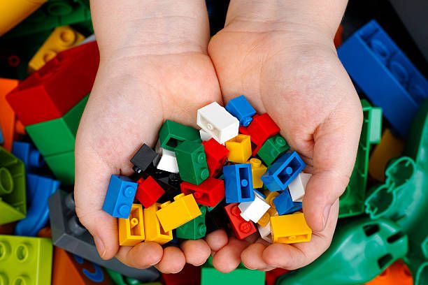 Colorful plastic LEGO toy building blocks held in outstretched hands showing primary colors on white background.