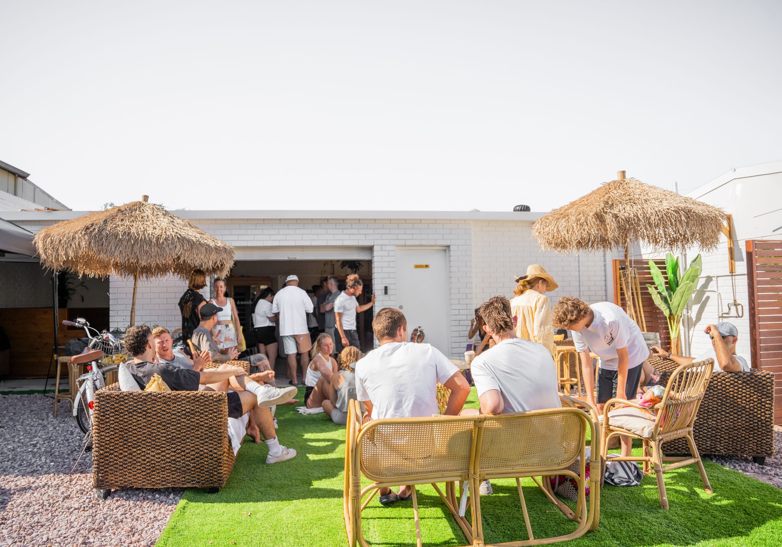 Outdoor lounge area with thatched umbrellas and wooden furniture on artificial grass.