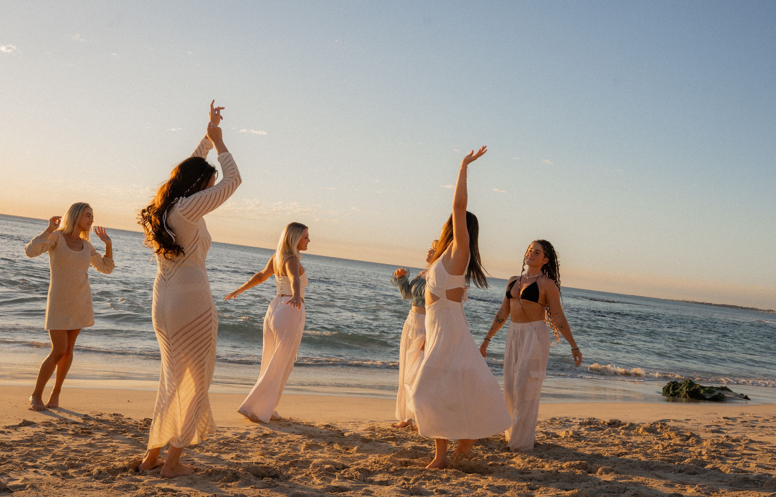 Group enjoying a sunset beach photoshoot while wearing coordinated white outfits.
