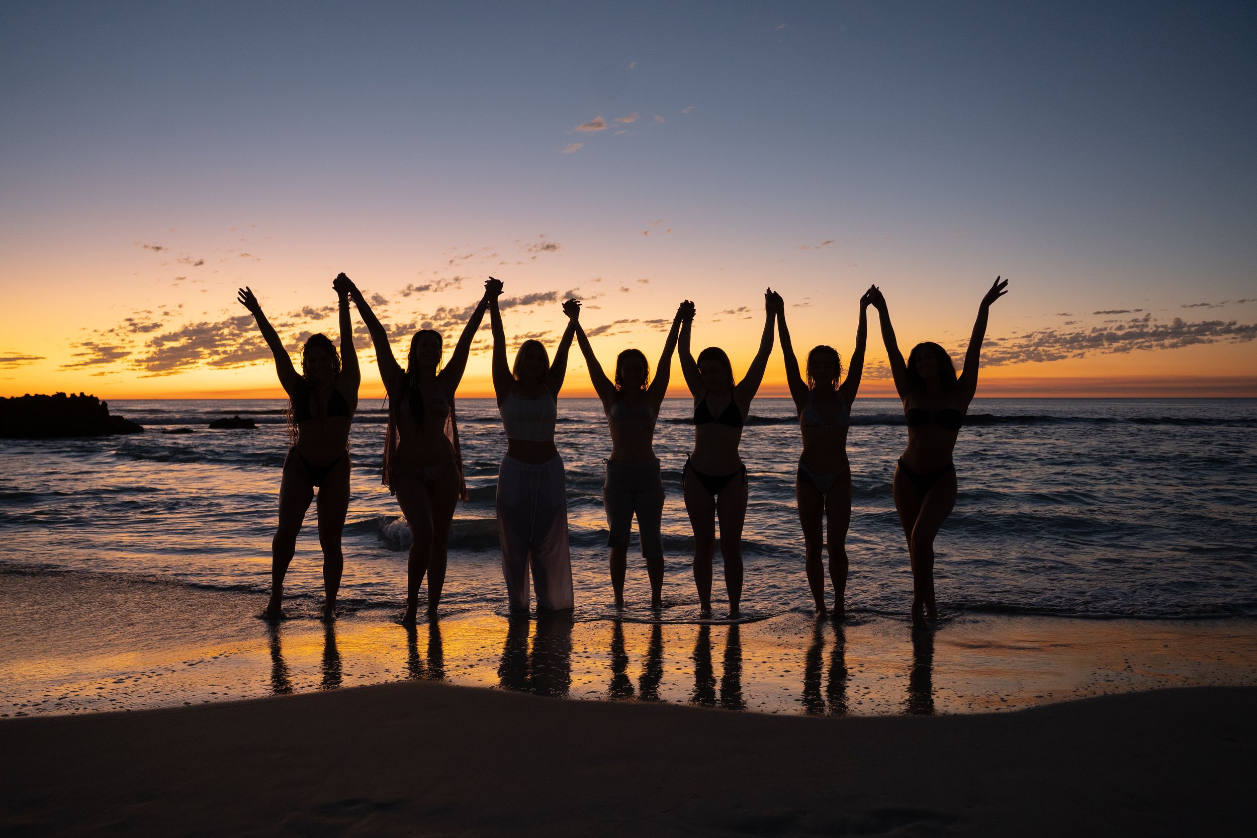 Silhouettes of people holding hands against a dramatic sunset beach backdrop.