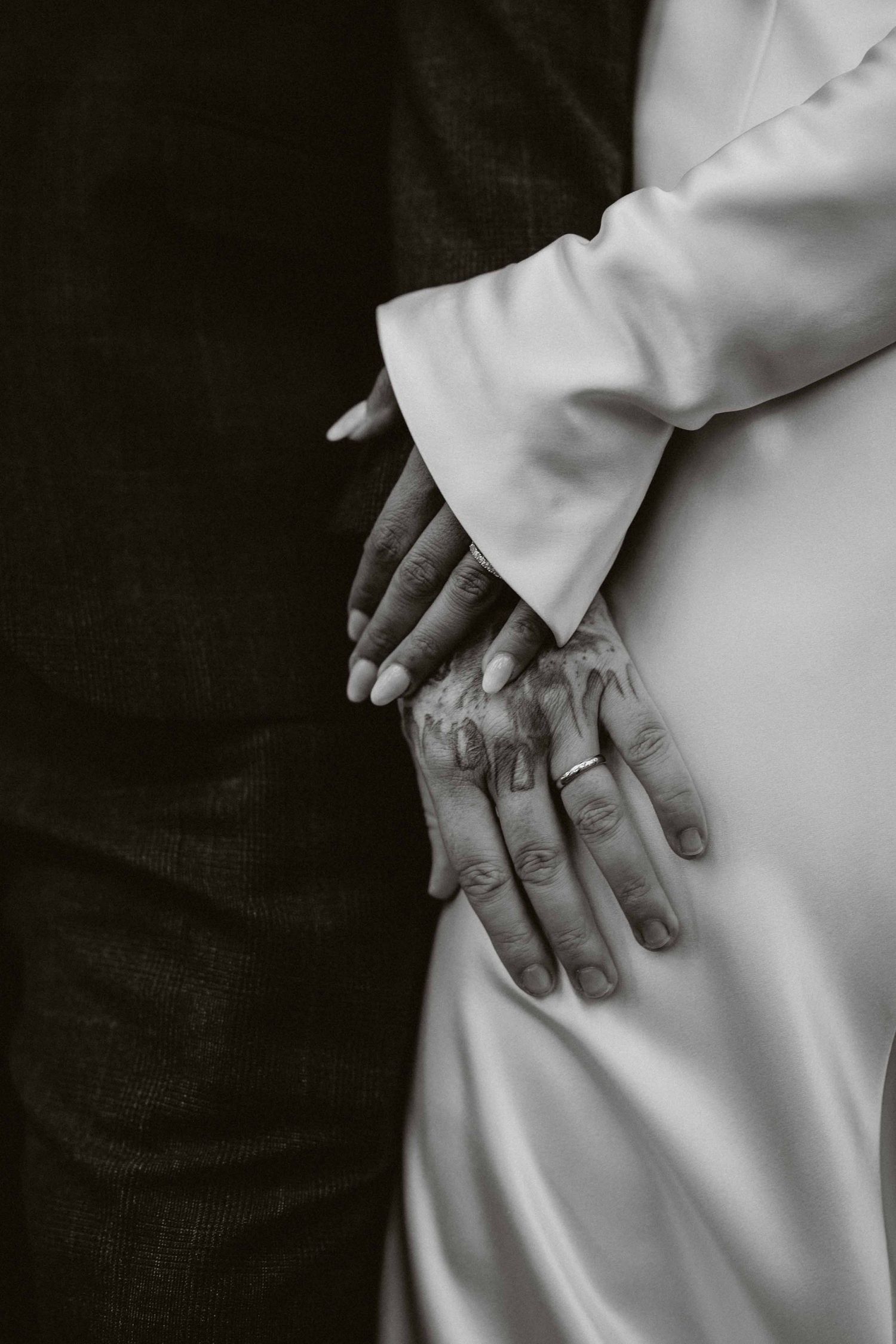 Black and white close-up photo showing two hands touching tenderly against white and dark clothing.