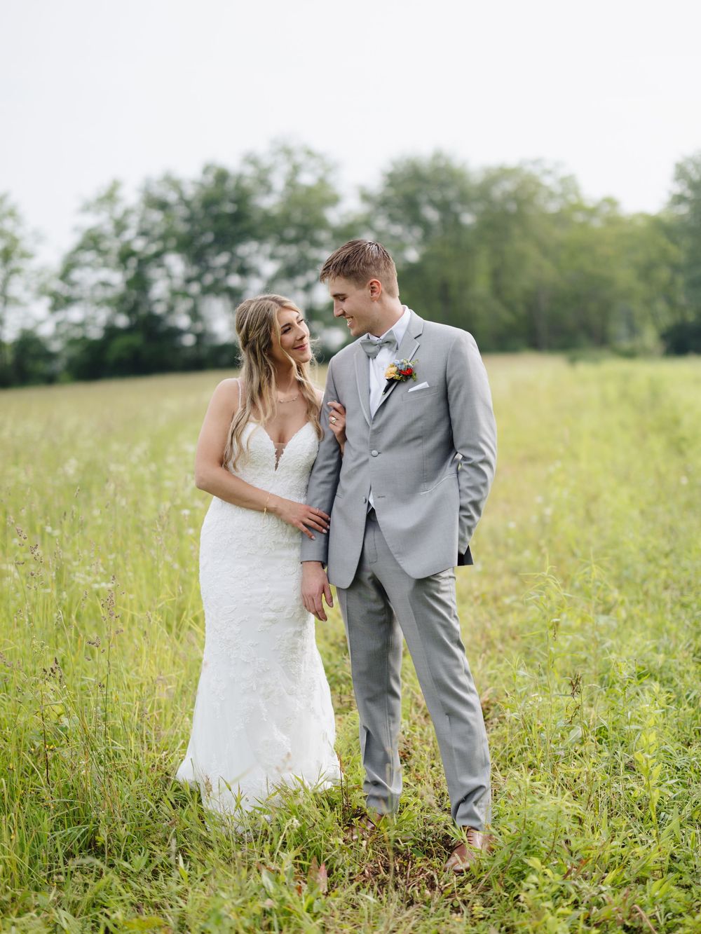 Wedding couple embraces and laughs together while standing in a sunlit meadow of tall grass.