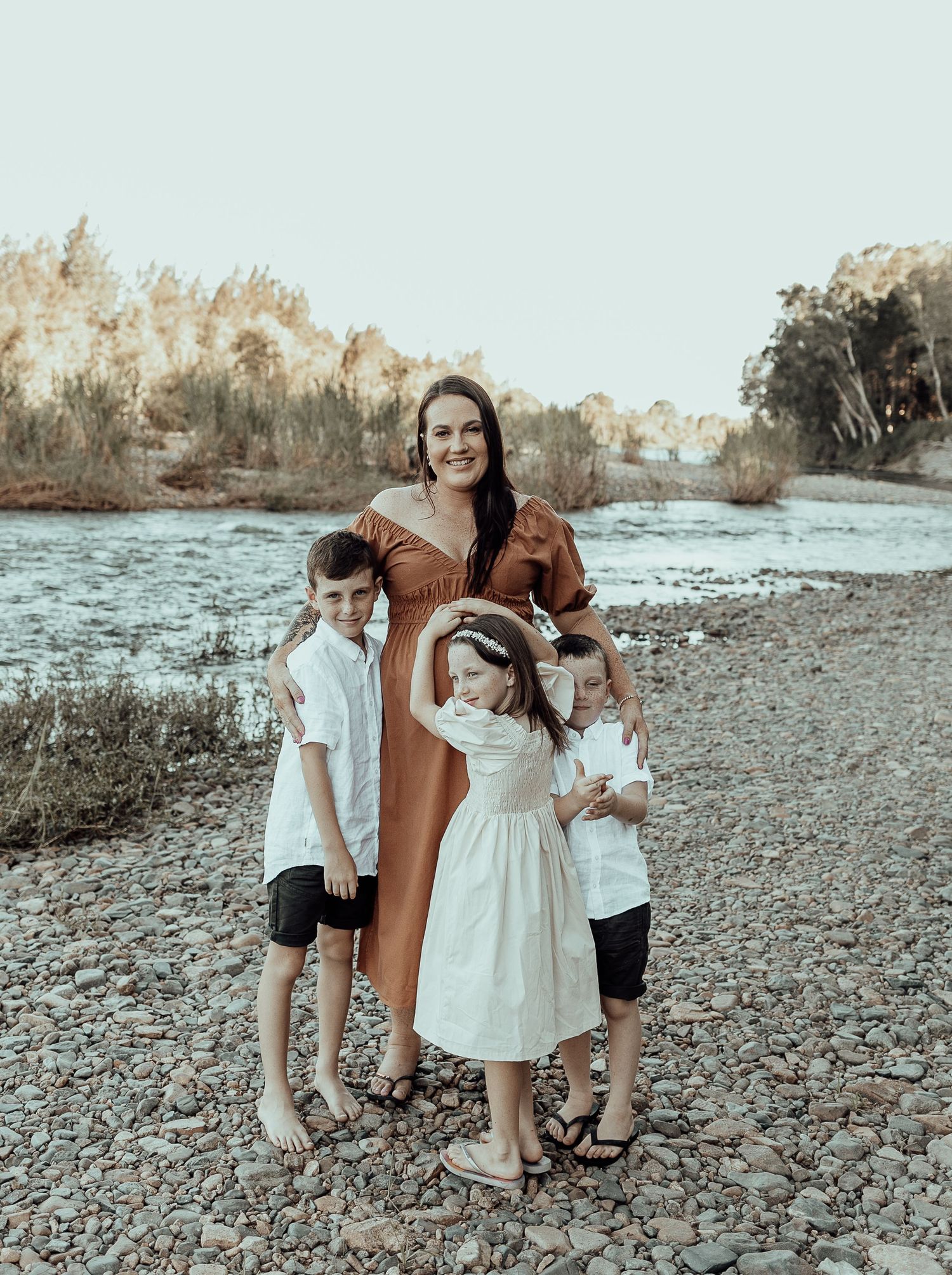 A muted toned photography series shows a caring moment between loved ones on a rocky riverbank.