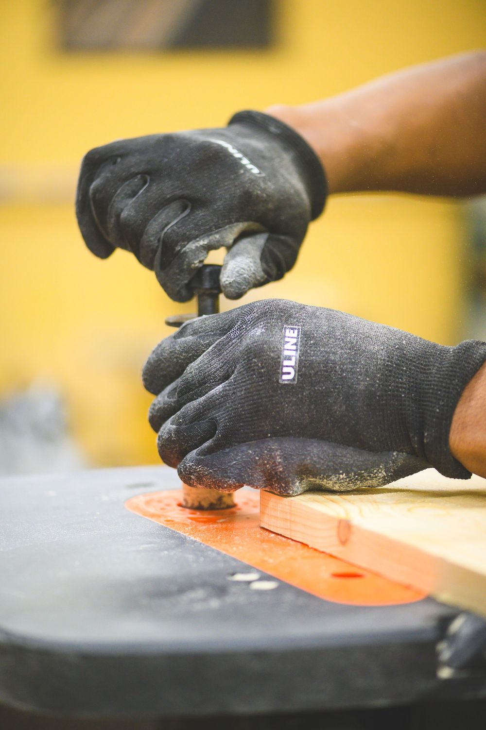 Close-up of hands wearing work gloves using woodworking tools.