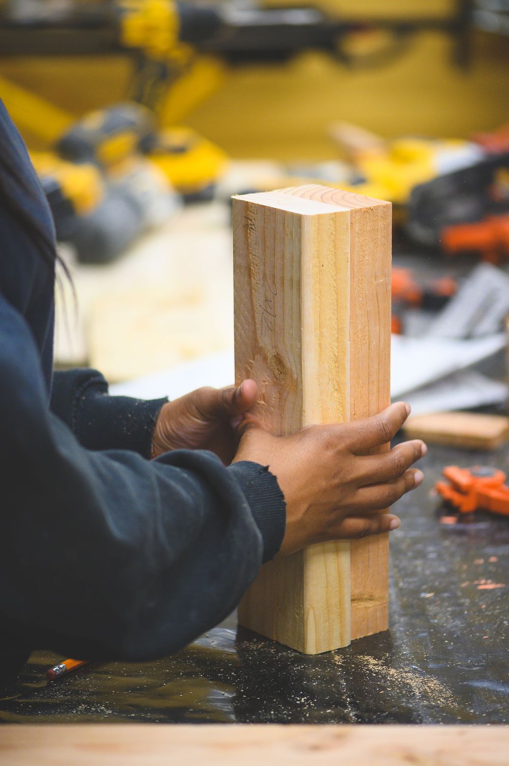 Hands holding a large wooden block in a workshop setting.