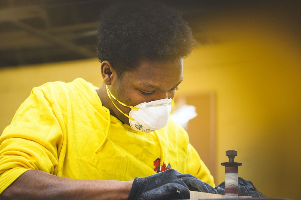 Person wearing yellow protective gear and face mask working in workshop.
