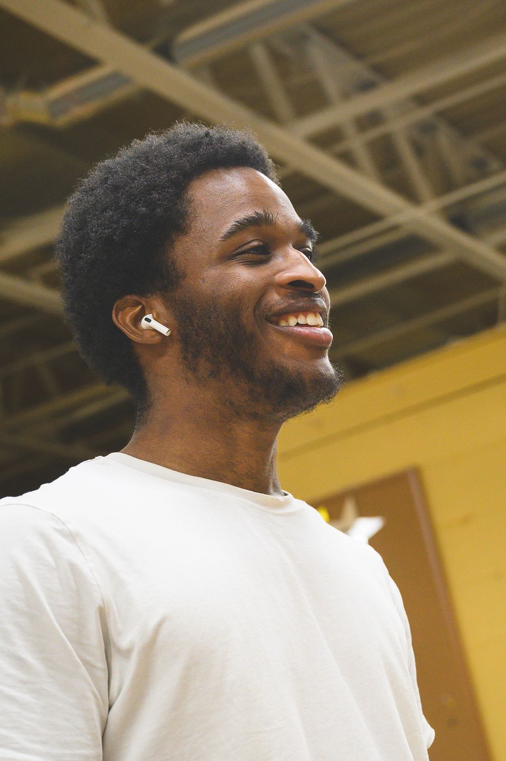 A person wearing white t-shirt and earbuds smiling.
