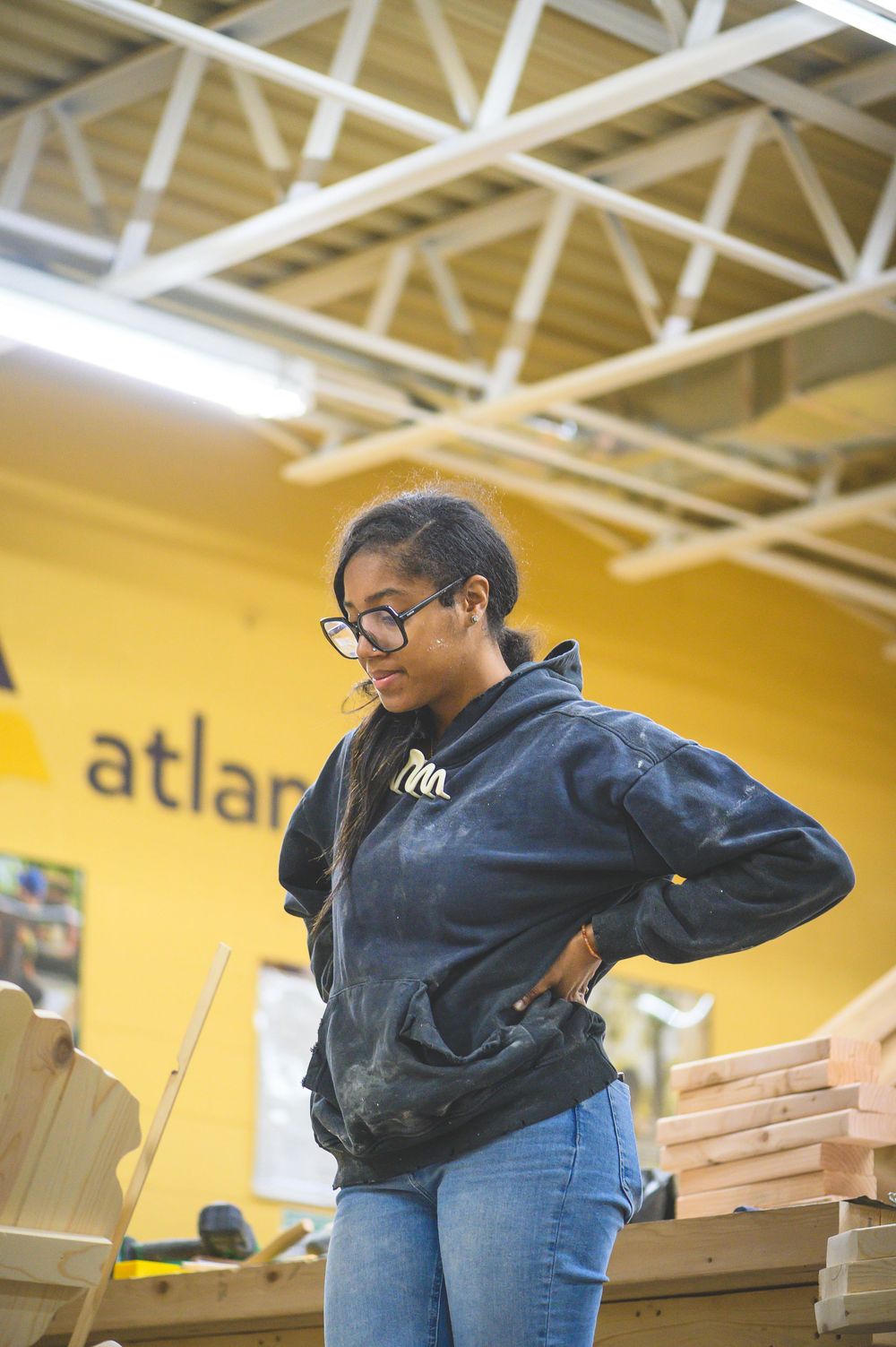 Person wearing navy blue sweater and jeans in warehouse space with yellow walls and exposed ceiling.