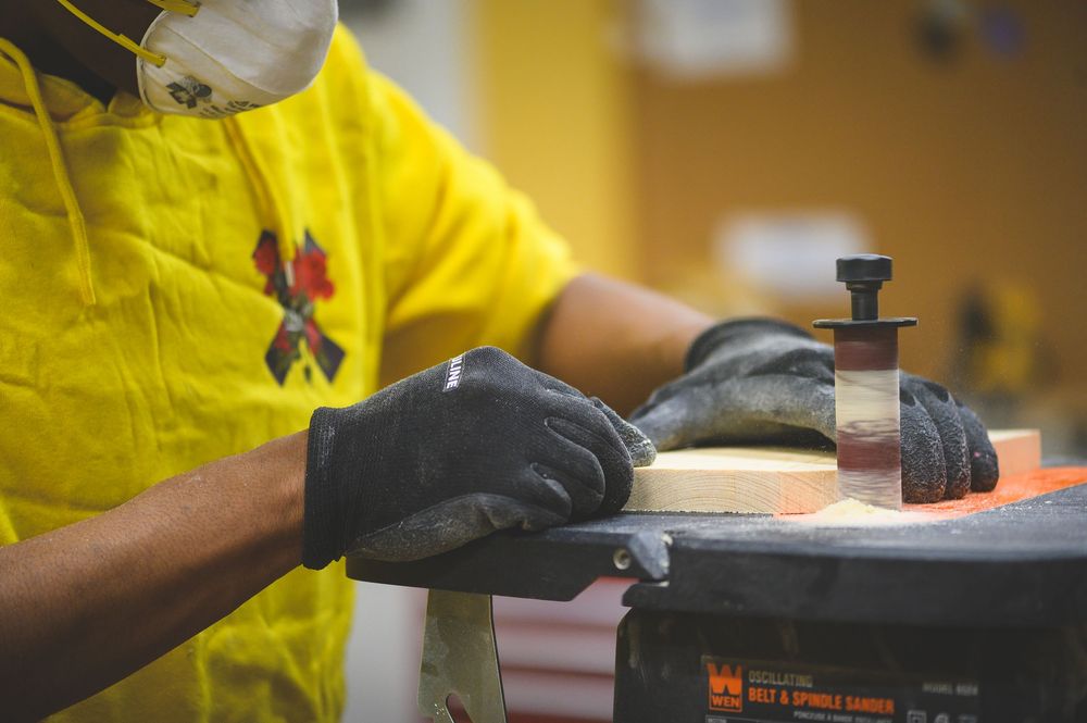 Close up of hands wearing yellow protective gloves working with tools and materials on a wooden surface.