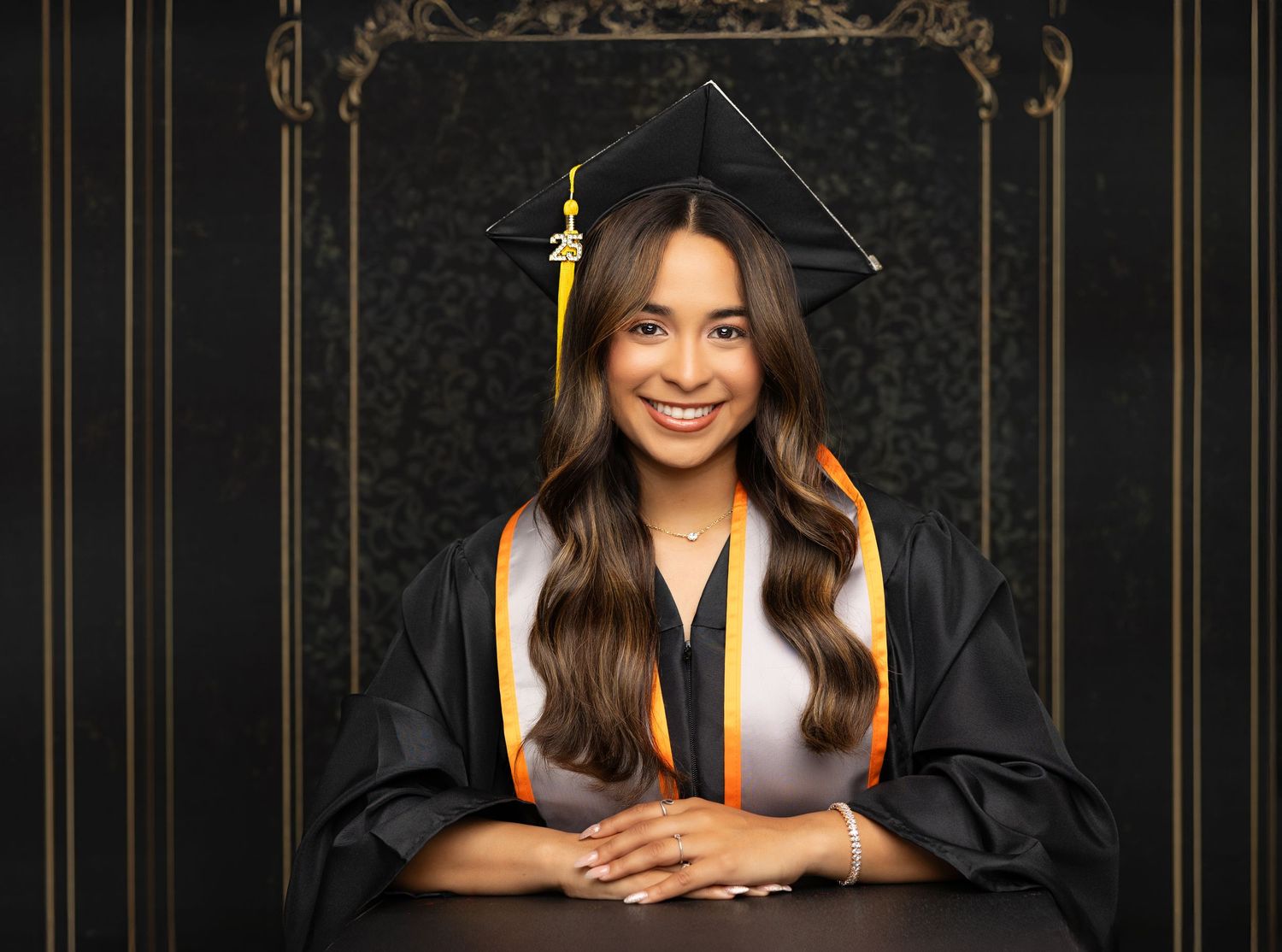 Graduate in cap and gown poses for professional portraits against a dark background with gold accents.