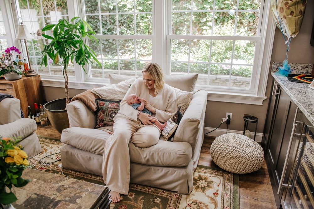 A bright sunroom decorated with cozy beige furniture, potted plants, and natural light streaming through large windows.