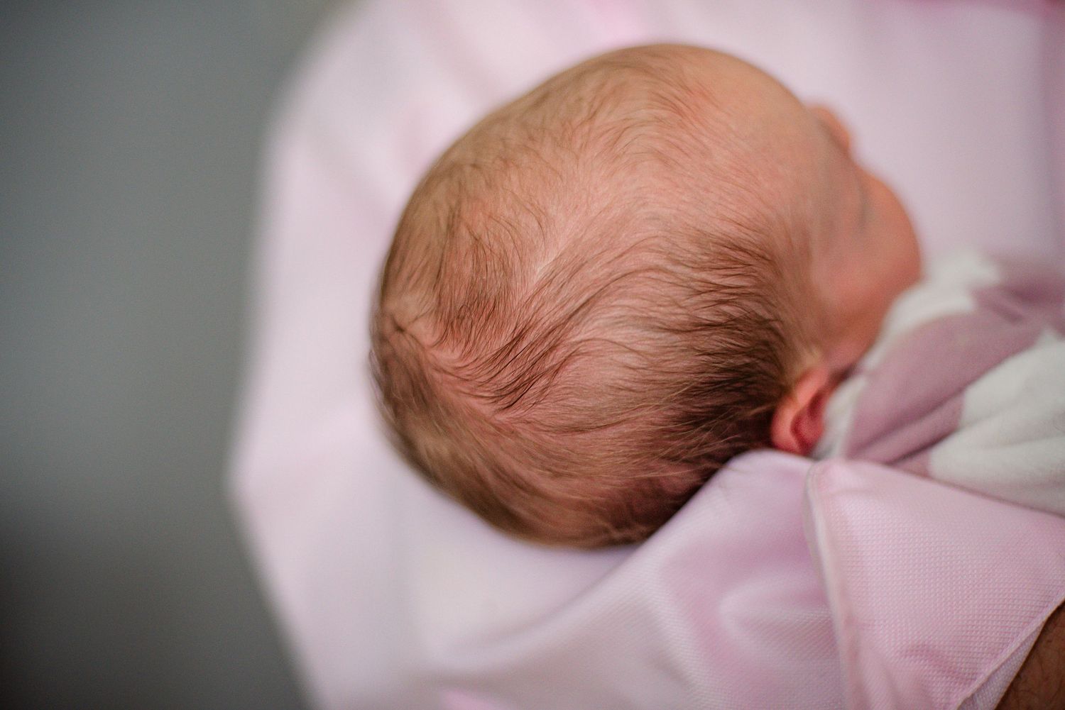 Close-up view of baby's head wrapped in soft pink blanket showing fine hair detail.