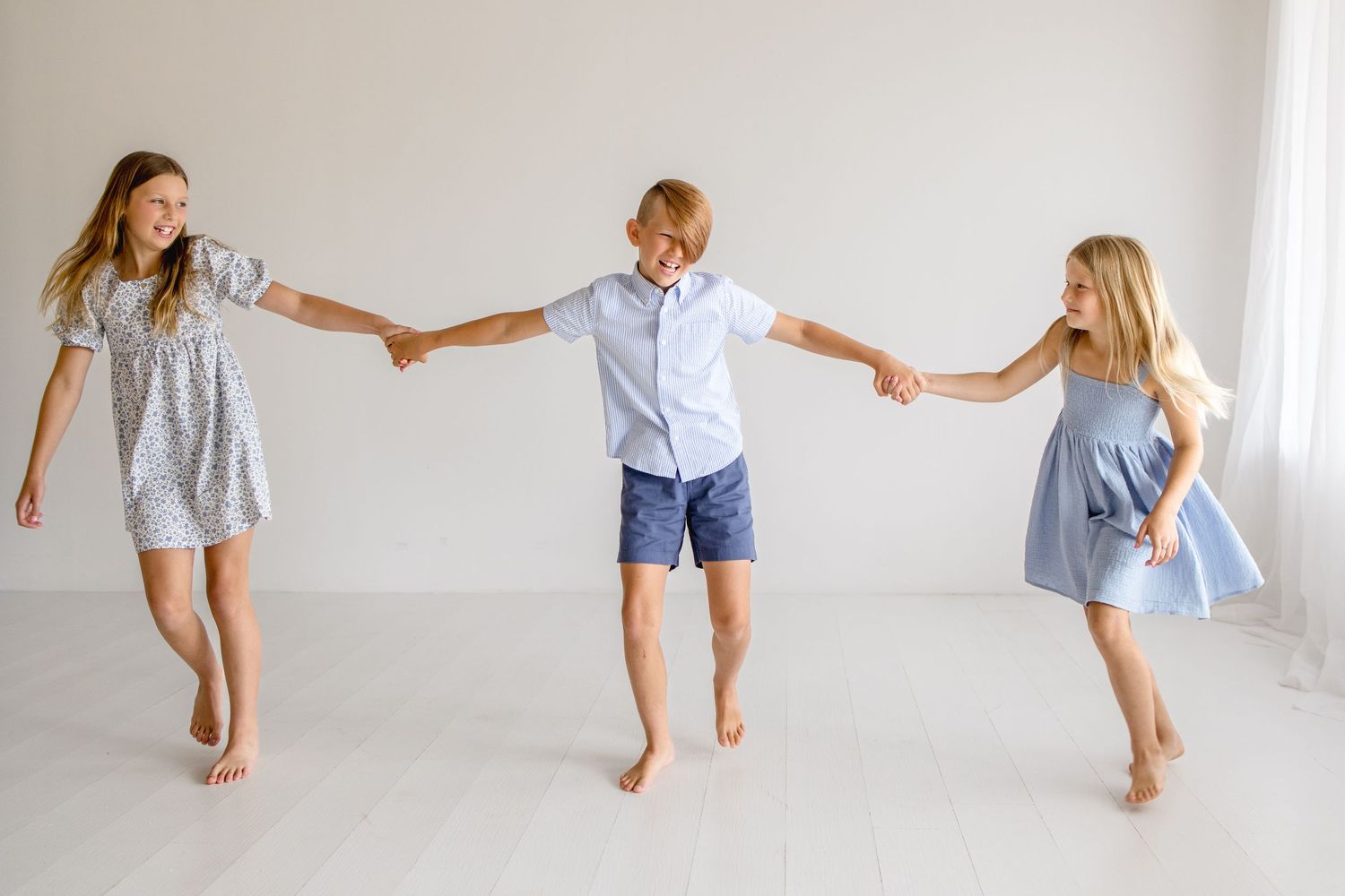 Three people hold hands while dancing in coordinated blue and white outfits against a white background.