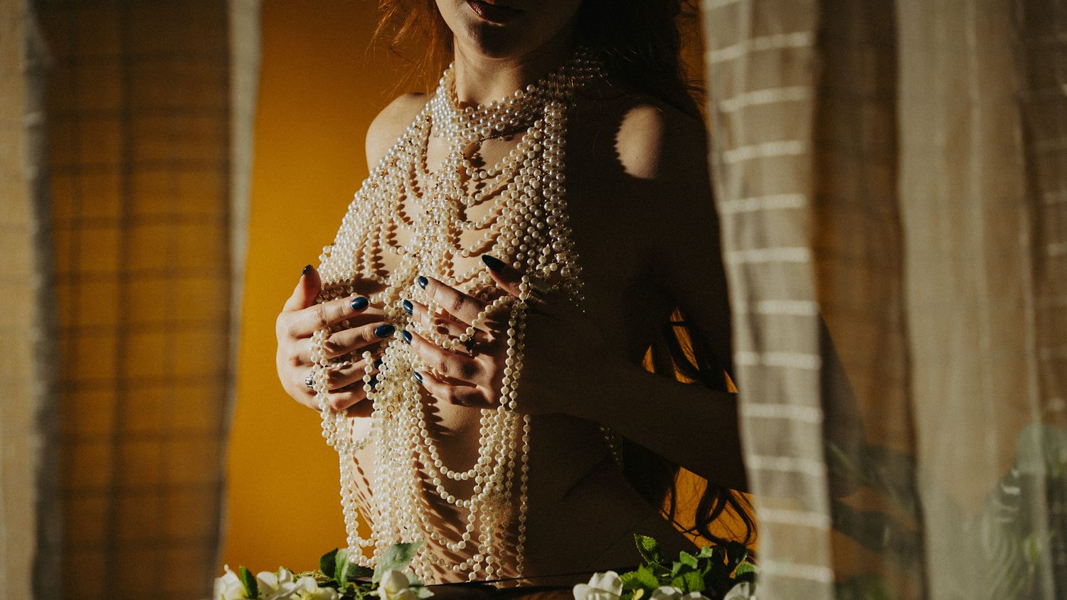 Warm dramatic portrait in moody lighting shows pearl necklace details in warm shadows against light background.