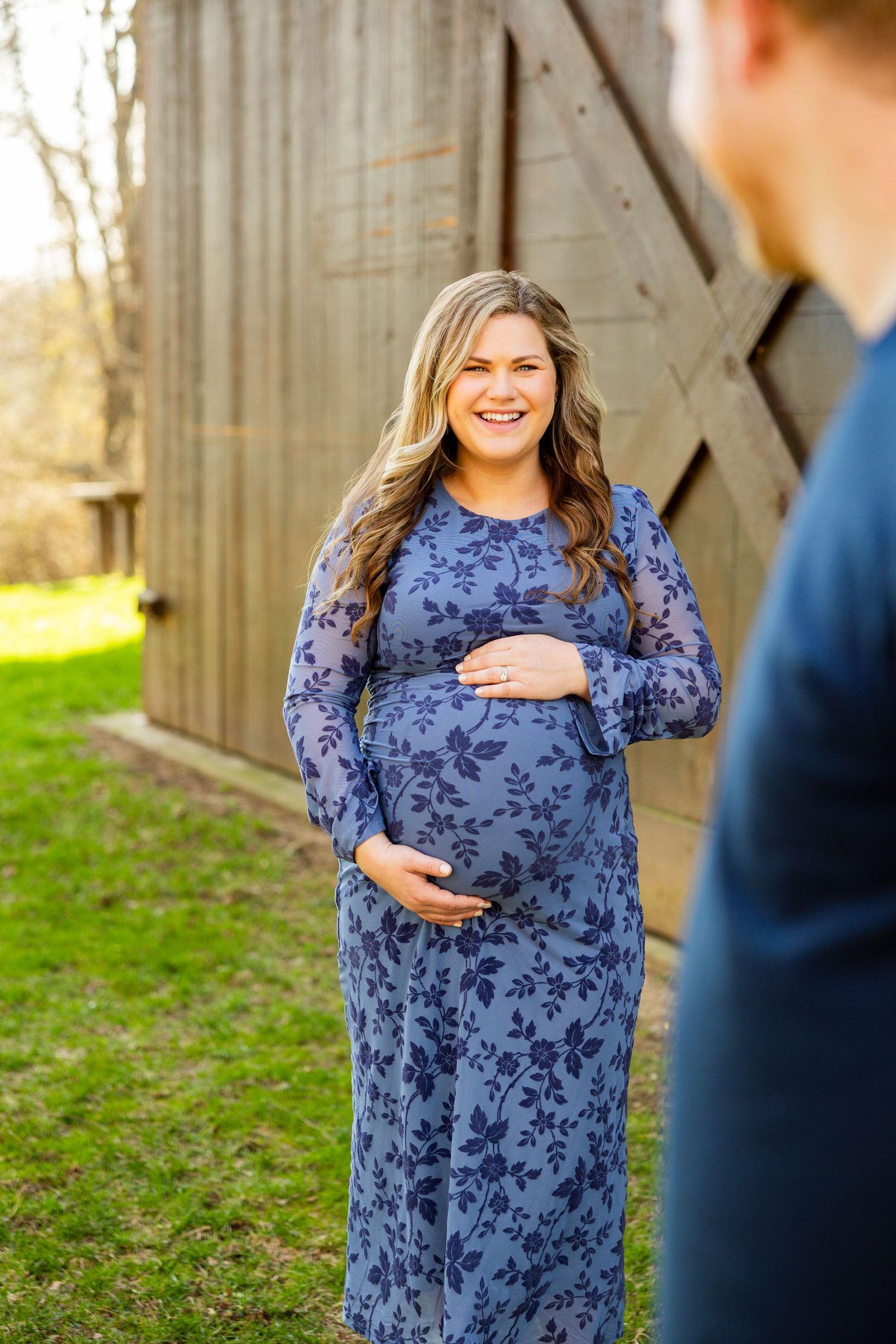 A person in a navy floral dress poses in front of a rustic wooden barn during a photo session.