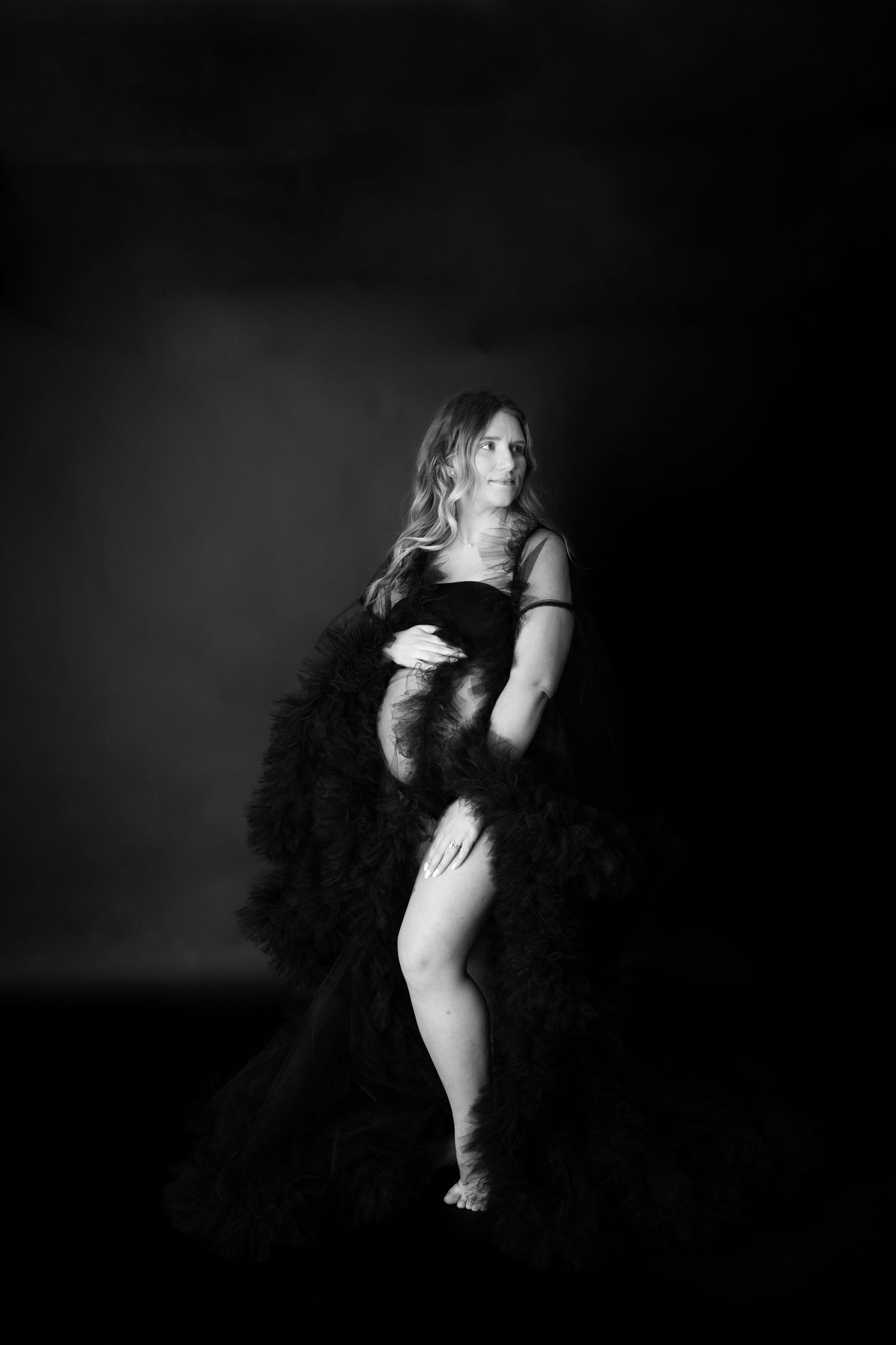 Dramatic black and white portrait of a dancer in a fluffy tulle dress posing against a dark background.