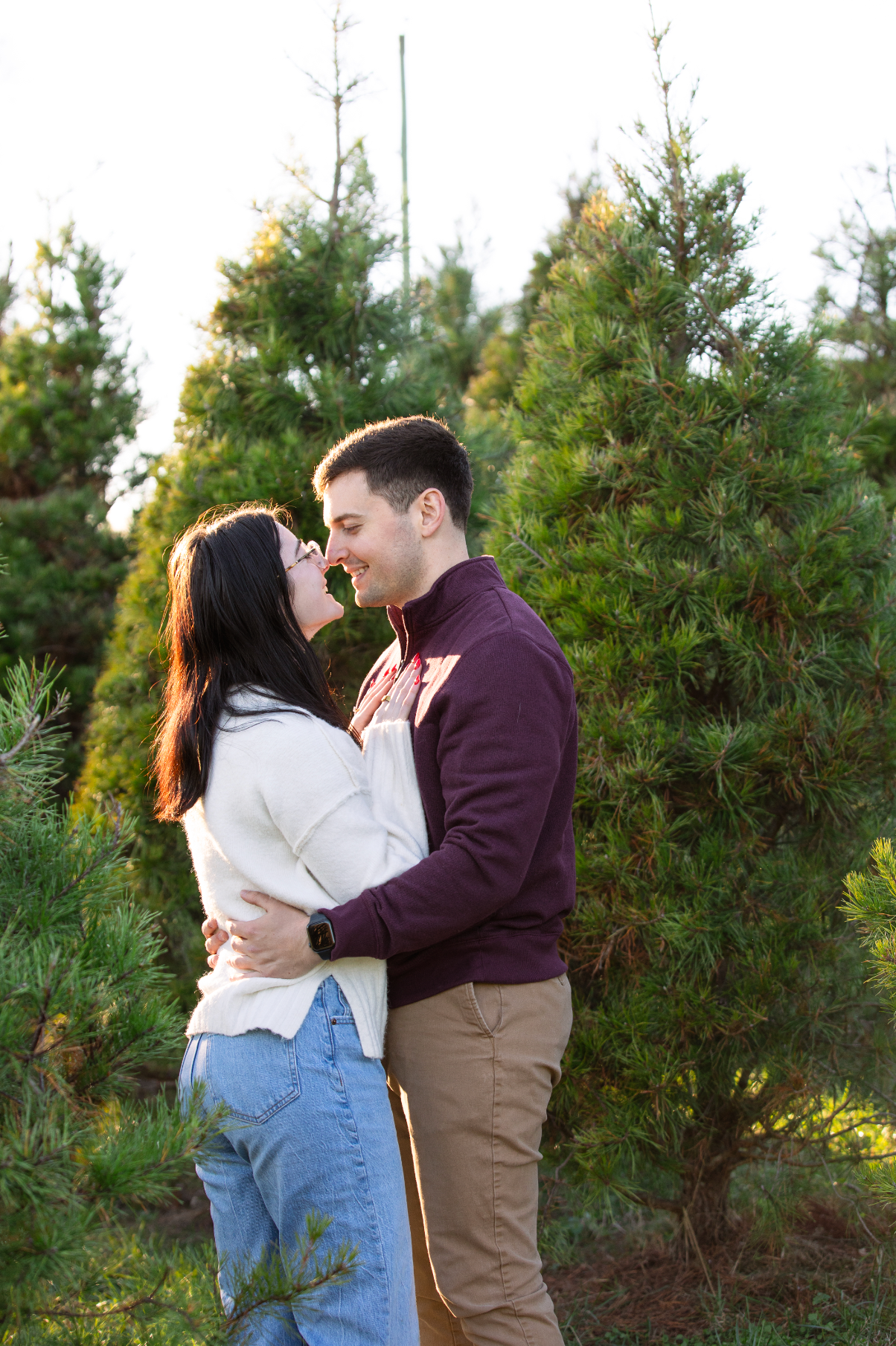 A romantic couple embraces in front of evergreen trees during a sunset photoshoot after getting engaged