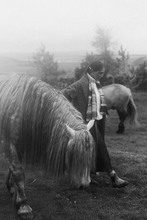 A person milking a shaggy Highland cow in a misty field, captured in a vintage black and white photograph.