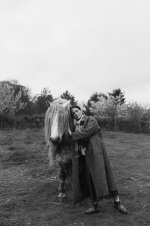 A black and white photo series showing someone in a long coat interacting with a white horse in a field.