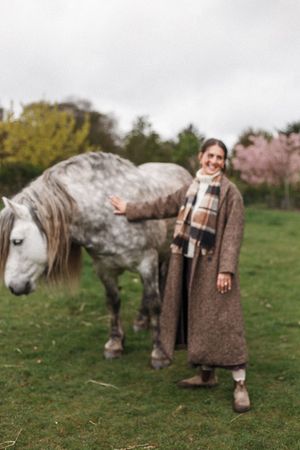 A color photo sequence showing someone in a tweed coat spending time with a dappled grey horse in a grassy field.