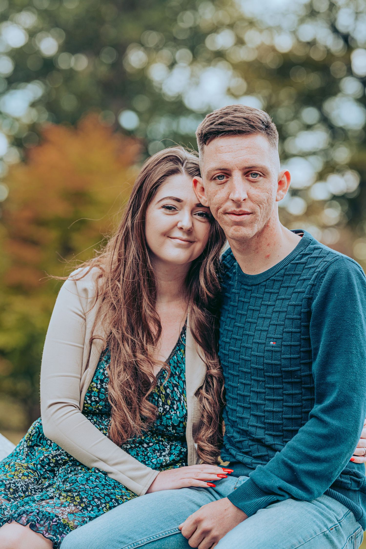 A couple sits together outdoors during autumn wearing teal and cream colored clothing in a romantic photoshoot.