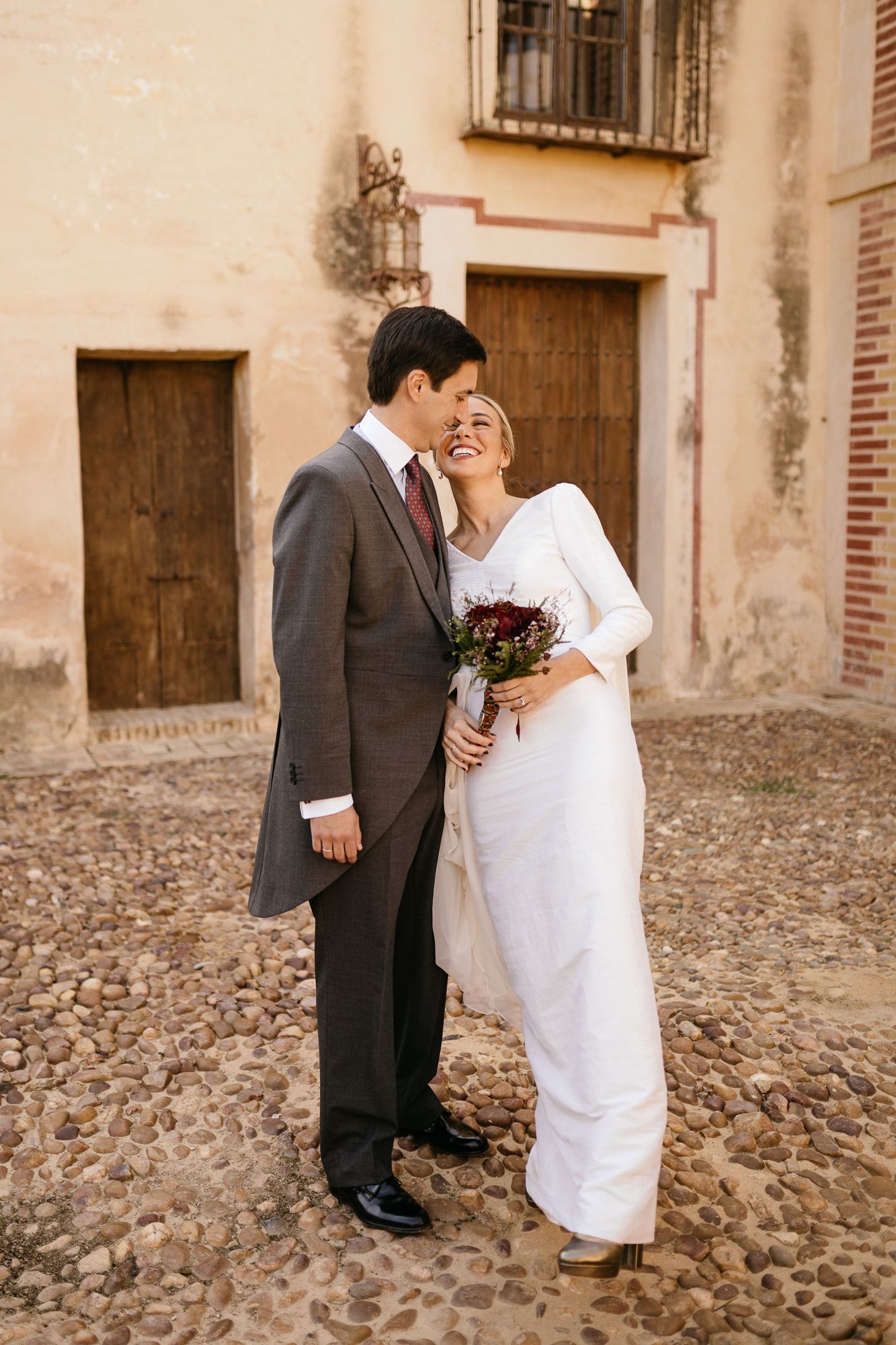 Couple sharing a romantic moment on cobblestone ground against a rustic building exterior.