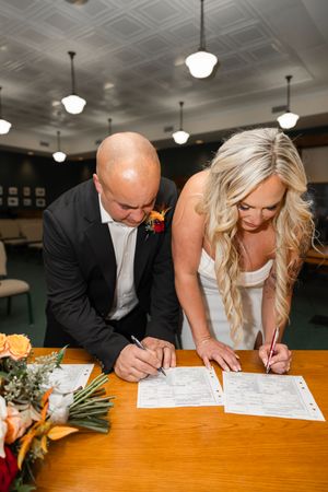 A couple signs their marriage license at a wooden table during their wedding ceremony. Northern NJ wedding photographer