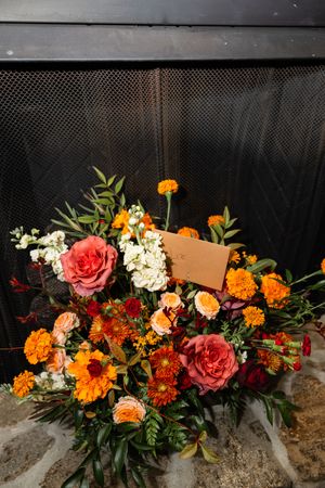 Vibrant floral arrangement with orange marigolds, pink roses, and white hydrangeas against a dark background. Northern NJ wedding photograph