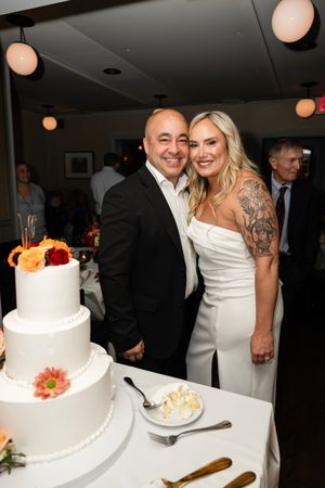 A couple poses together next to their white tiered wedding cake - Northern NJ wedding photographer