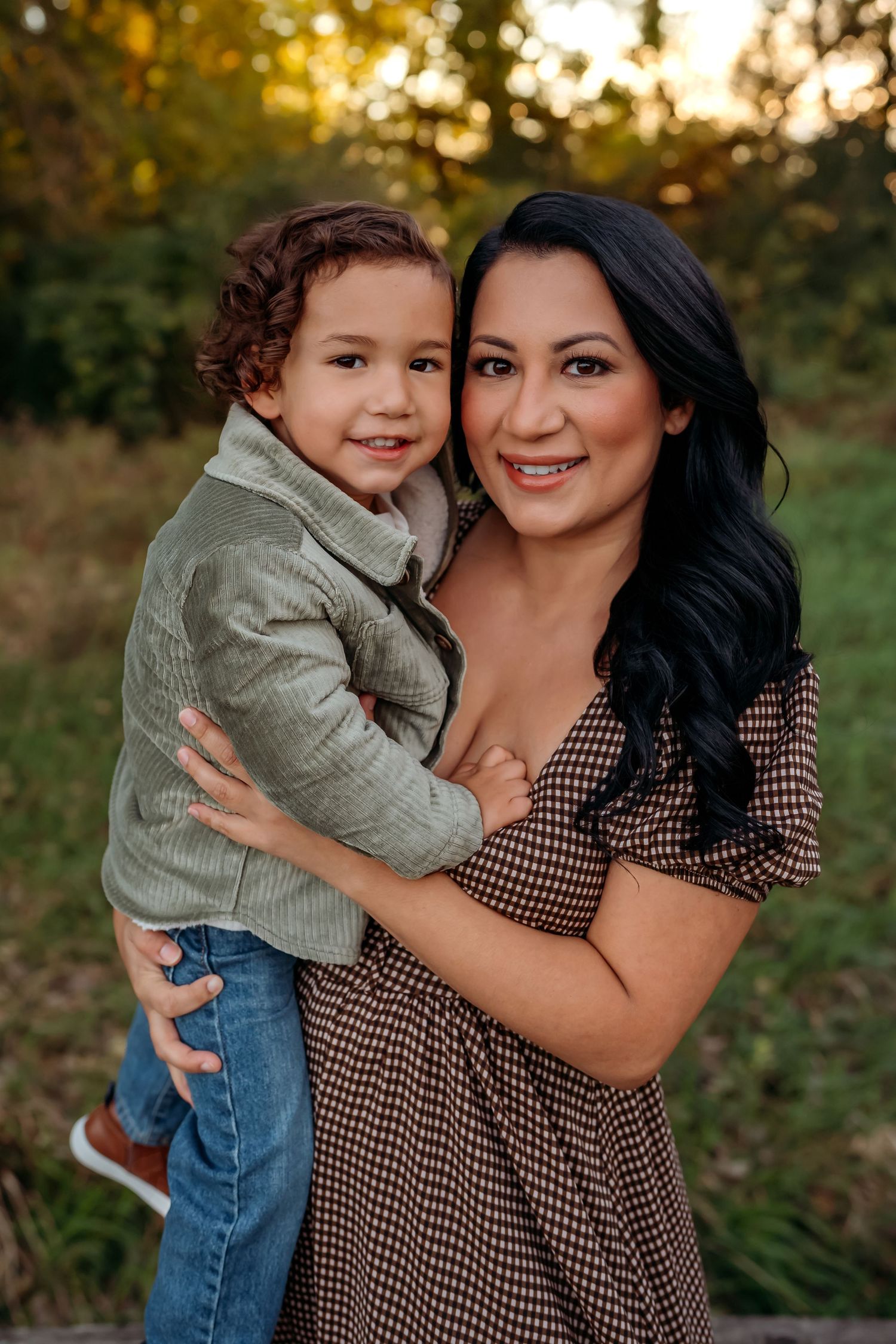 A mother and child pose together outdoors at sunset wearing coordinating casual outfits in a natural setting.