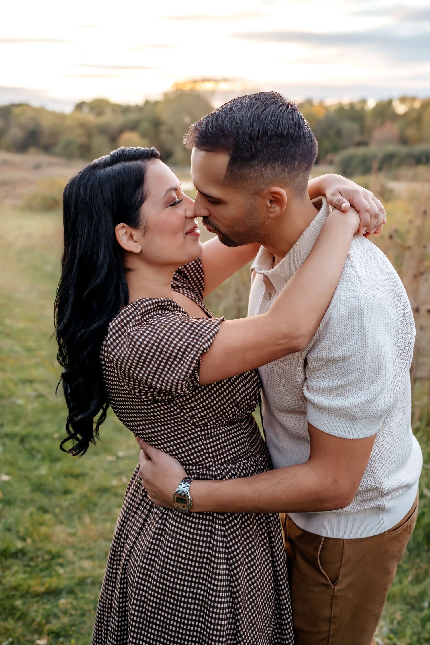 Romantic couple embracing and sharing a tender kiss in a sunlit meadow at golden hour.