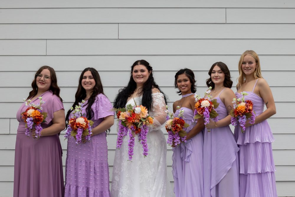 Bride and bridesmaids lined up smiling at the camera holding their bouquets.