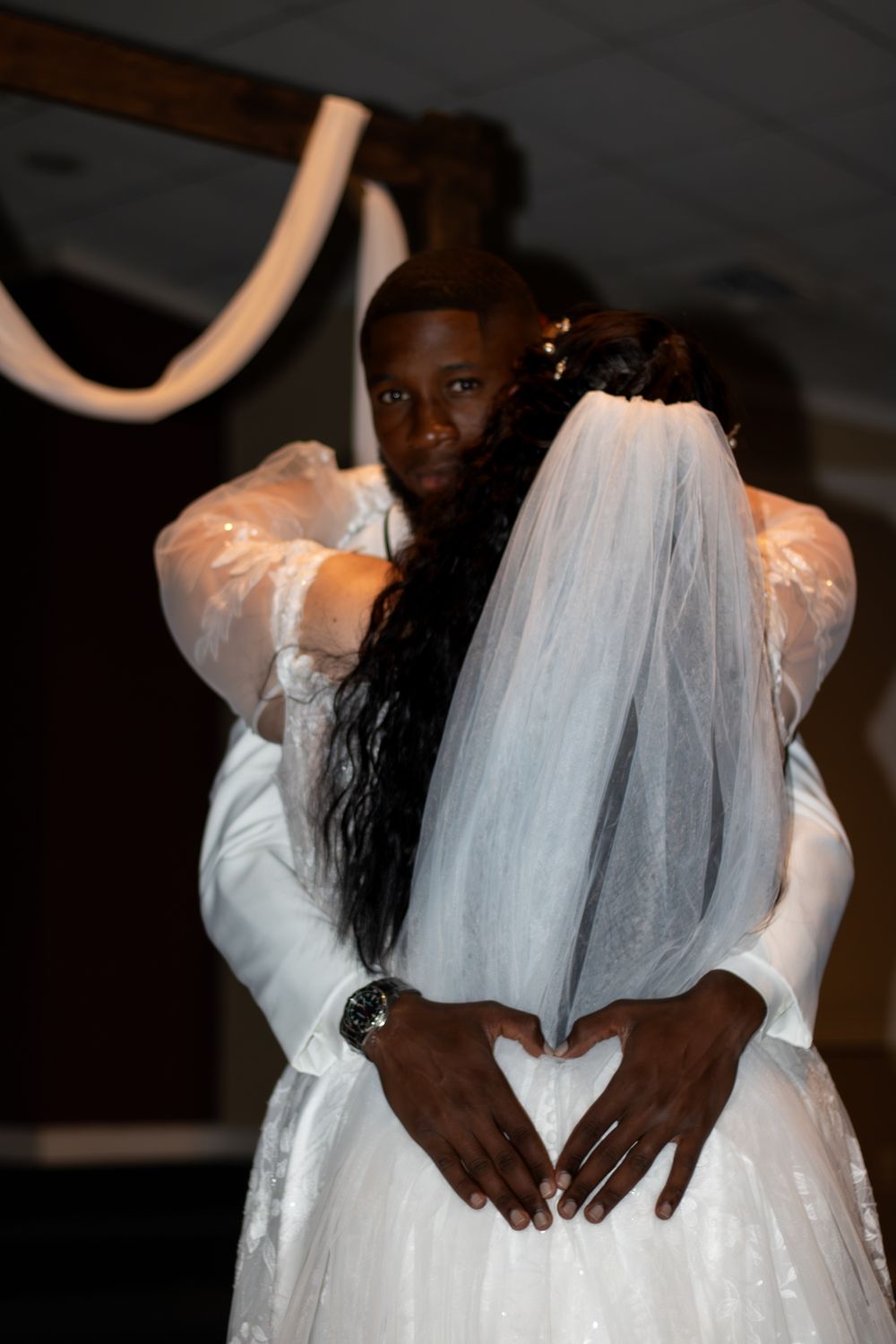 Groom holding a heart on brides back while looking at the camera.