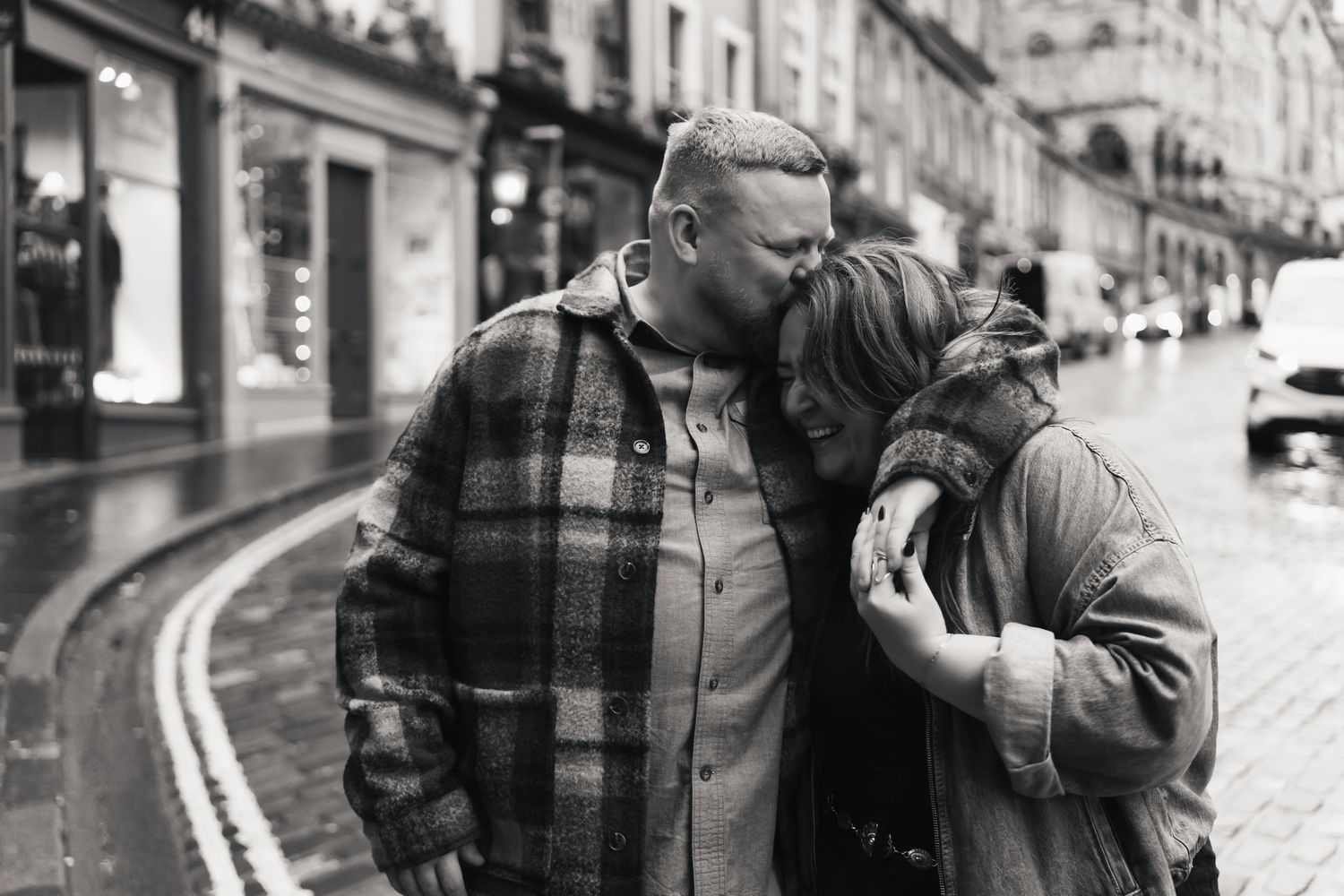 Black and white street photography shows a couple embracing in front of a building facade.