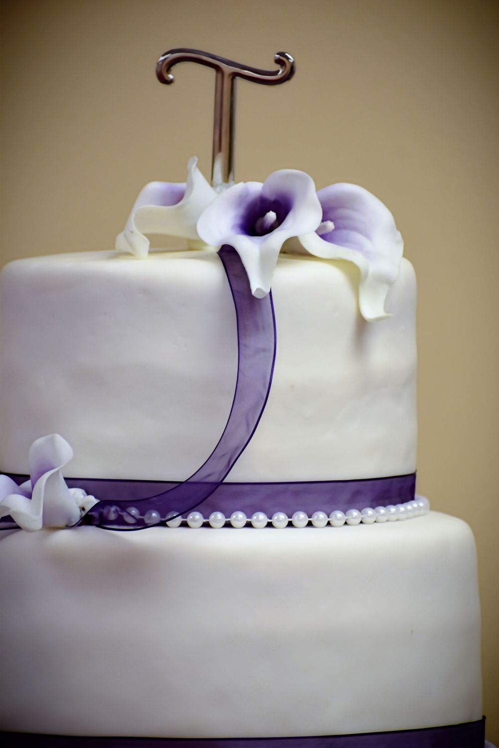 Close-up photos showing white fondant wedding cake details with purple ribbon trim and pearl accents.