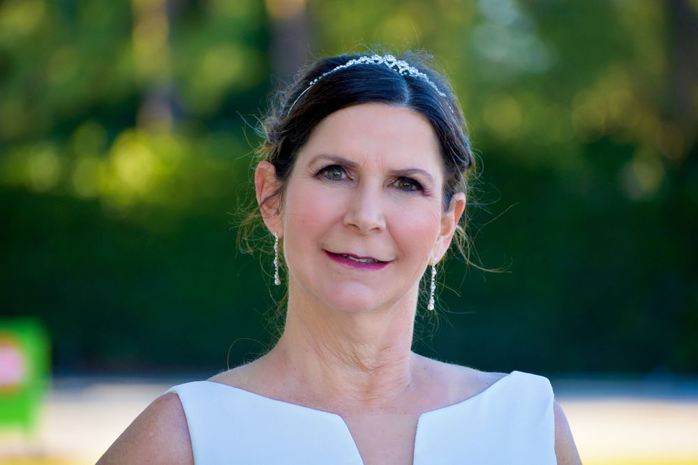 A person in formal attire stands outdoors with a blurred green background and natural lighting.