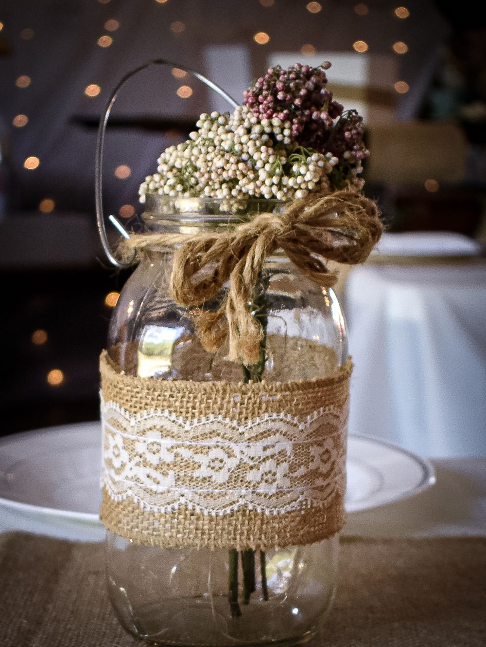 Mason jars decorated with rustic burlap and white lace trim displayed as wedding centerpieces with baby's breath flowers.