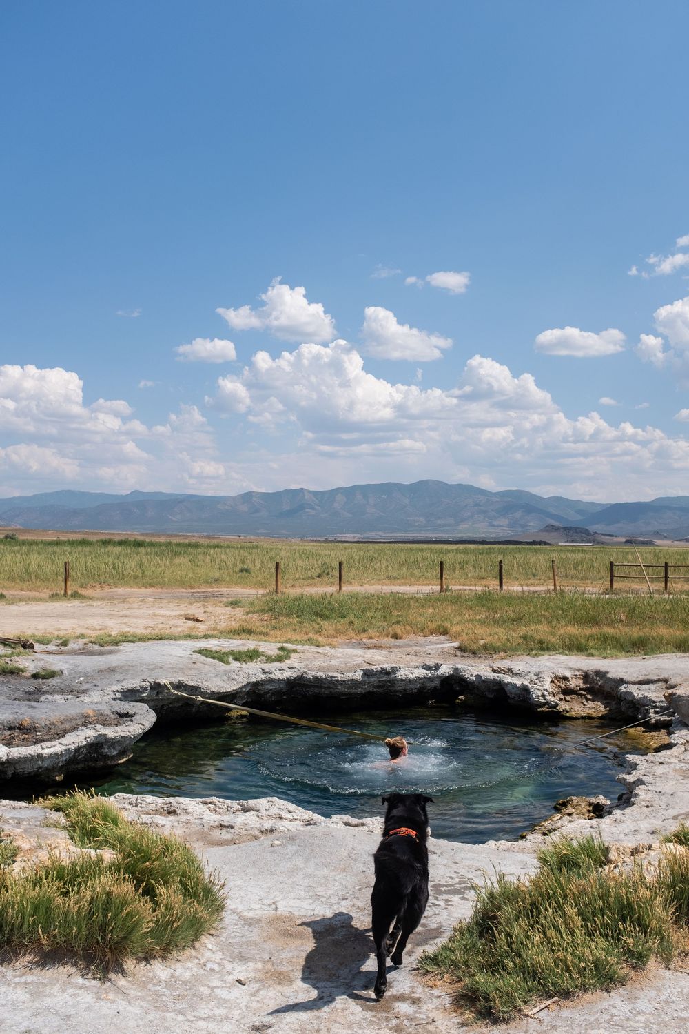 Hot springs and thermal pools in a desert landscape with mountains visible in the distance under blue skies.