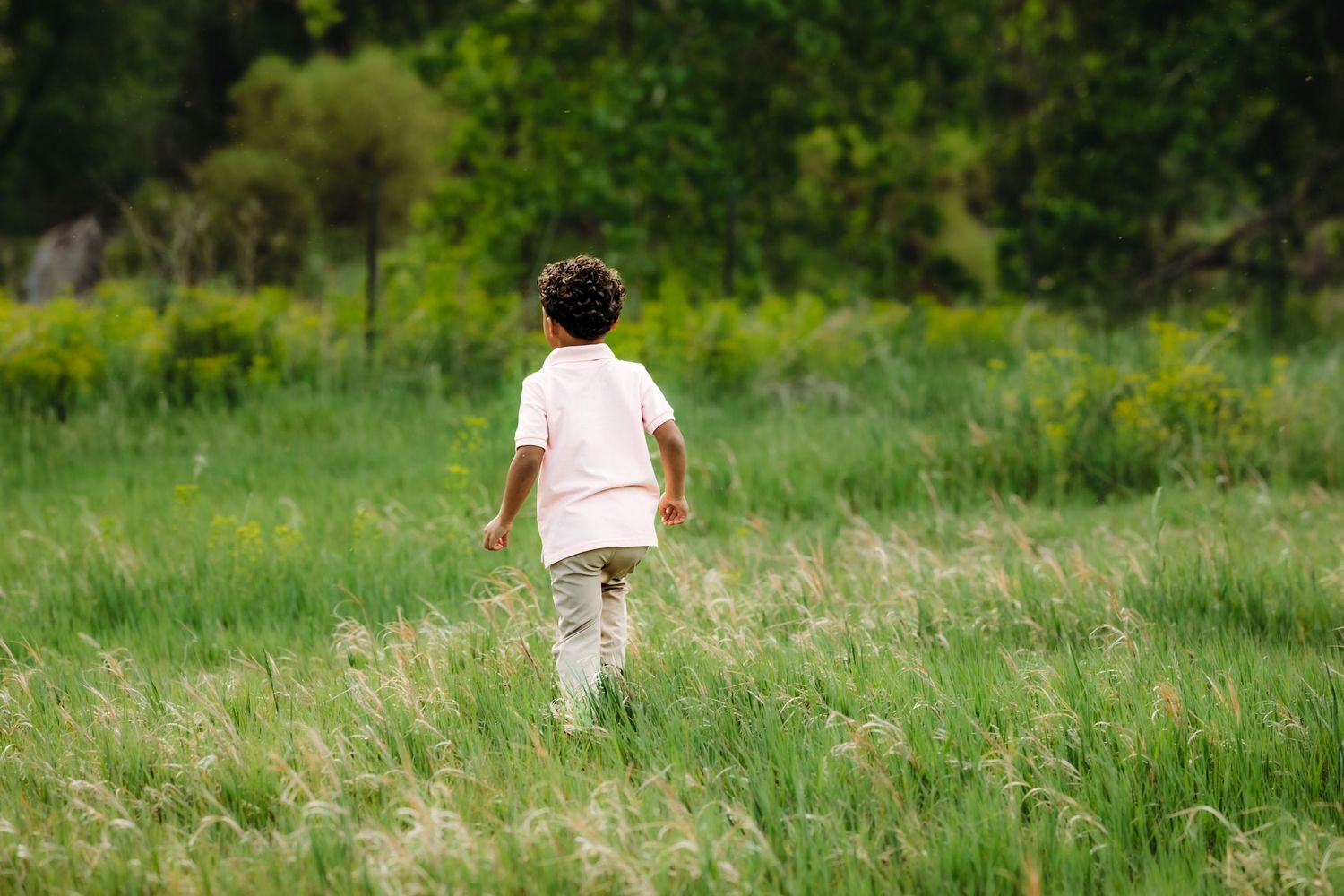 A small figure in a white shirt runs through a lush green meadow on a sunny summer day.