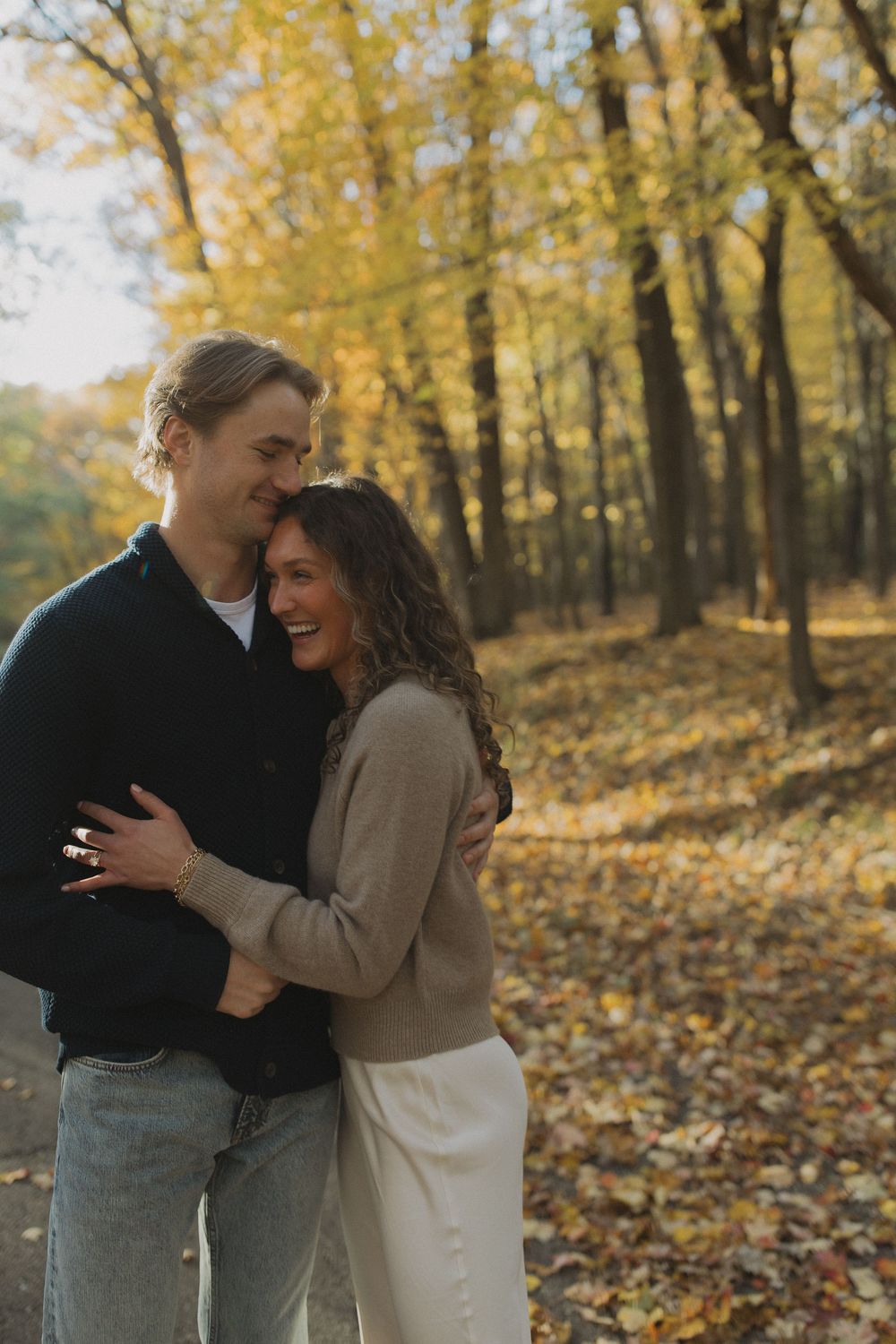 A joyful autumn engagement moment captured among yellow-leaved trees.