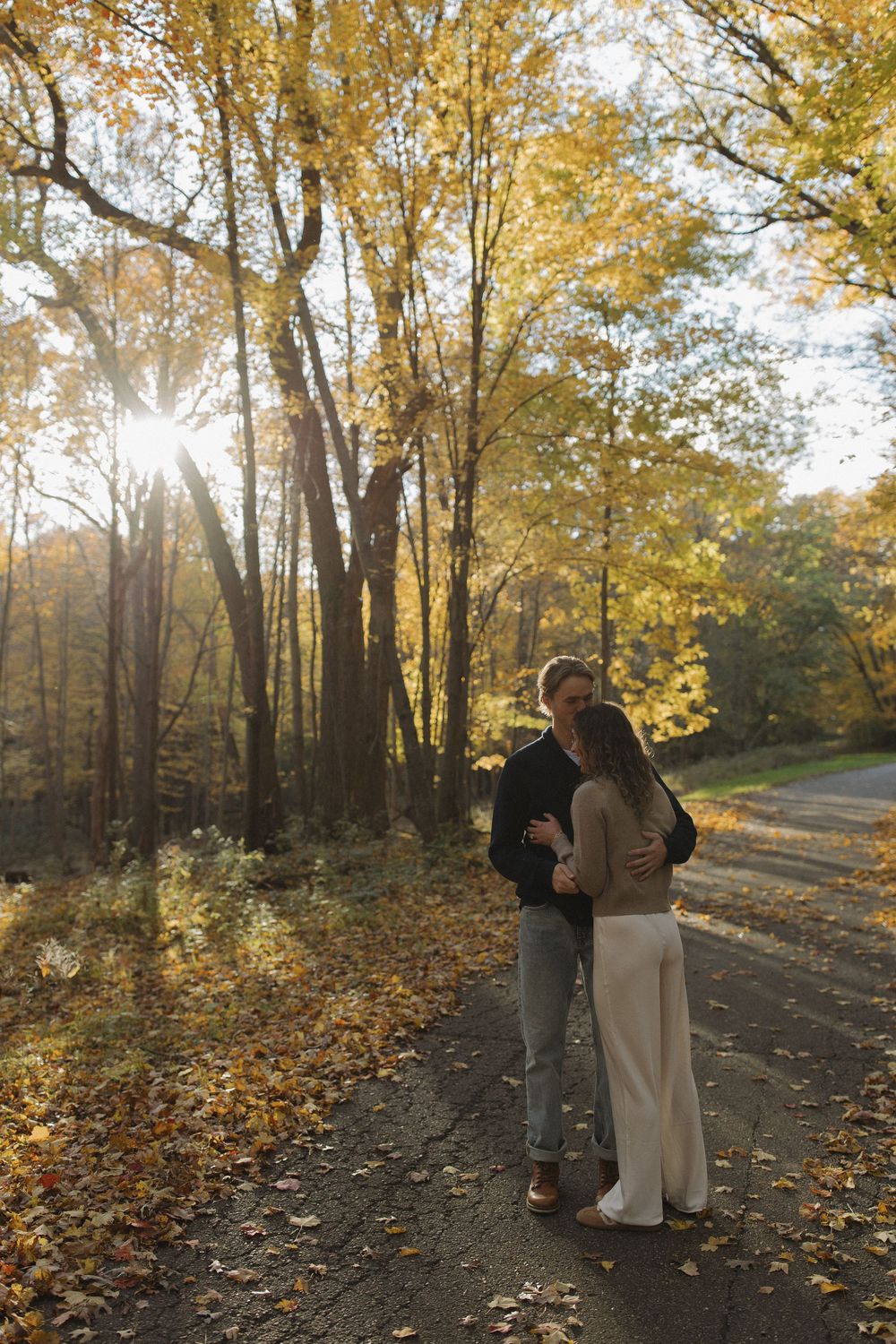 A couple embracing on a sunlit forest path surrounded by golden autumn foliage.