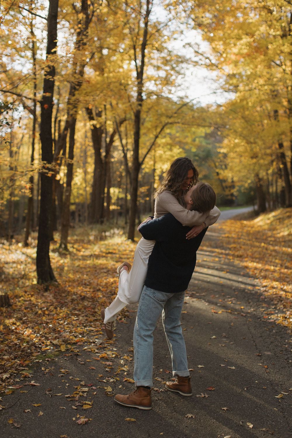 A romantic embrace on a forest path surrounded by golden fall foliage.